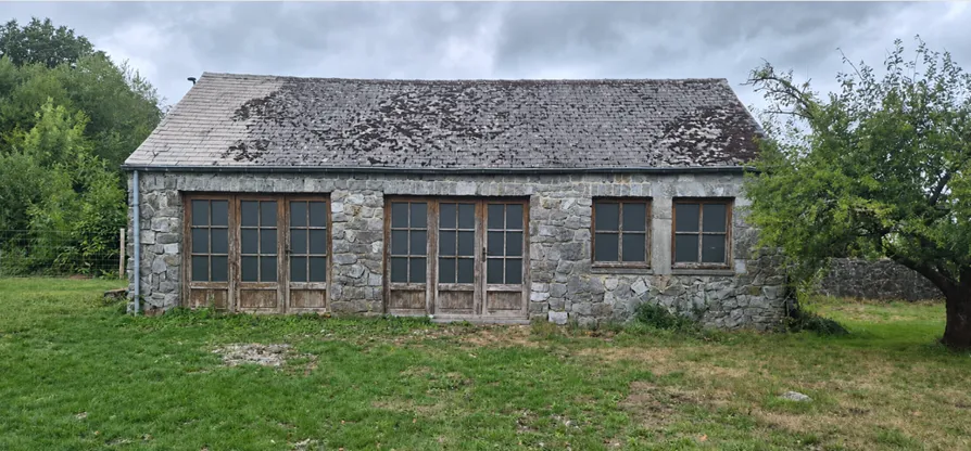 Le garage d'origine : une petite dépendance en pierre, aux portes et châssis de bois, isolée dans un pré.